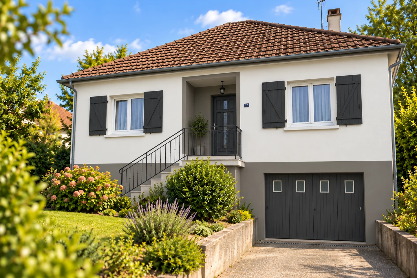 Façade blanc cassé avec soubassement gris et volets anthracite sur une maison des années 70–80